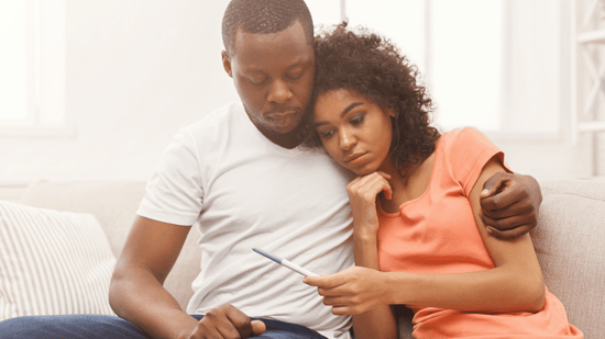 african american couple sitting looking down at pregnancy test 