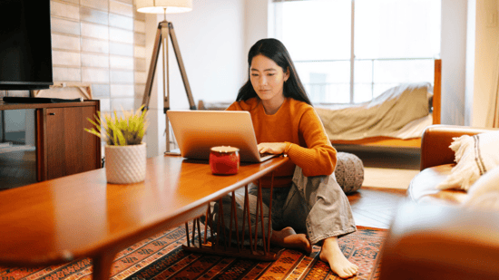 asian woman sitting at end of coffee table on floor looking at laptop with crossed legs