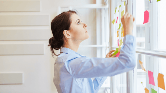 woman in light blue long sleeve top and hair in bun looking up at window and colored sticky notes
