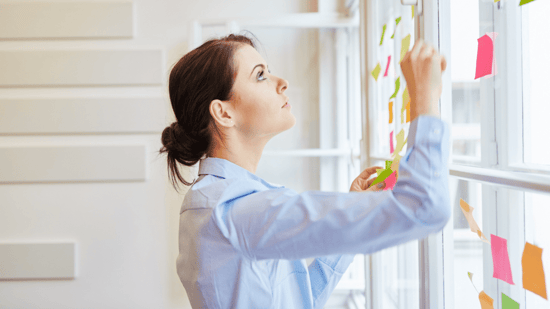 woman in light blue long sleeve top and hair in bun looking up at window and colored sticky notes