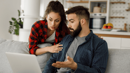 woman with hair in ponytail hands on arm of man gesturing and looking at a laptop computer